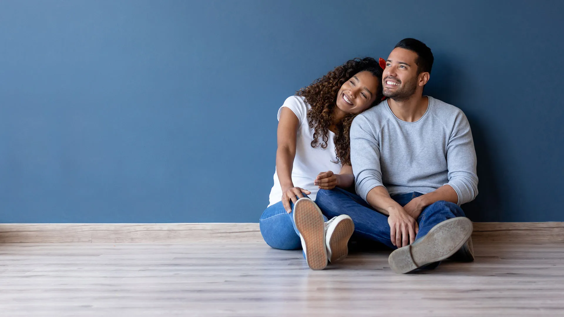 Hero image. A couple sitting on the floor against the wall of their unfurnished new home.